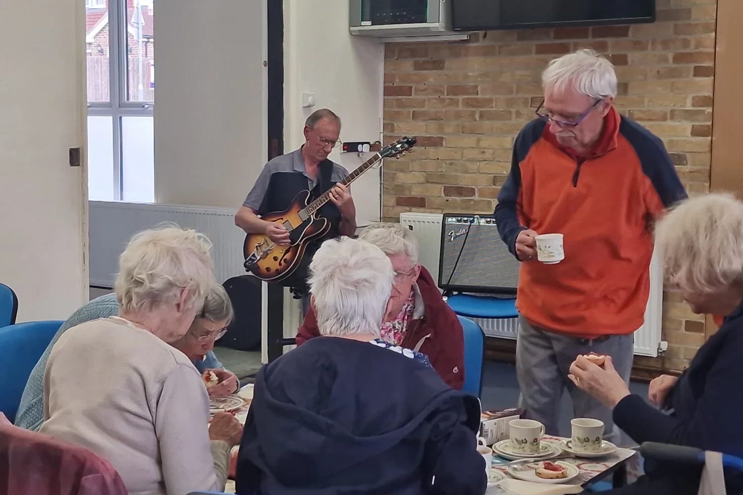 Rotarian Barry Ednie chats to local senior citizens at an annual Country Drive and Cream Tea while Mike Golding entertains them on guitar
