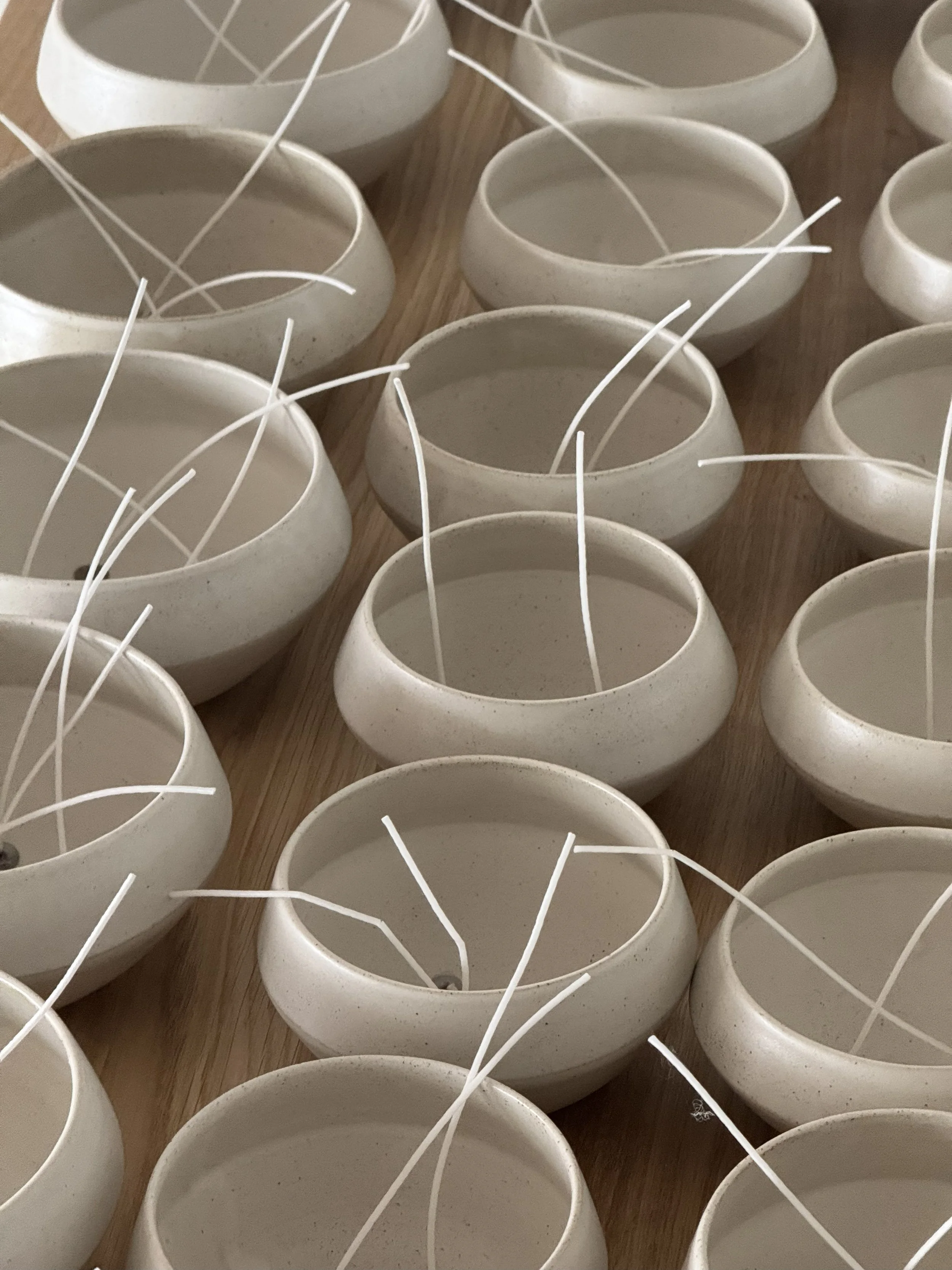 Multiple unlit white ceramic candles with wicks on a wooden surface