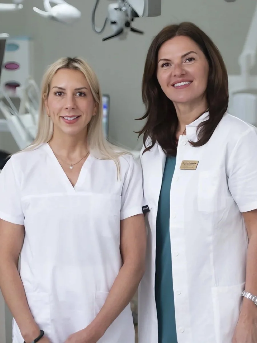 Två kvinnliga sjuksköterskor i vita kläder i ett medicinskt rum.