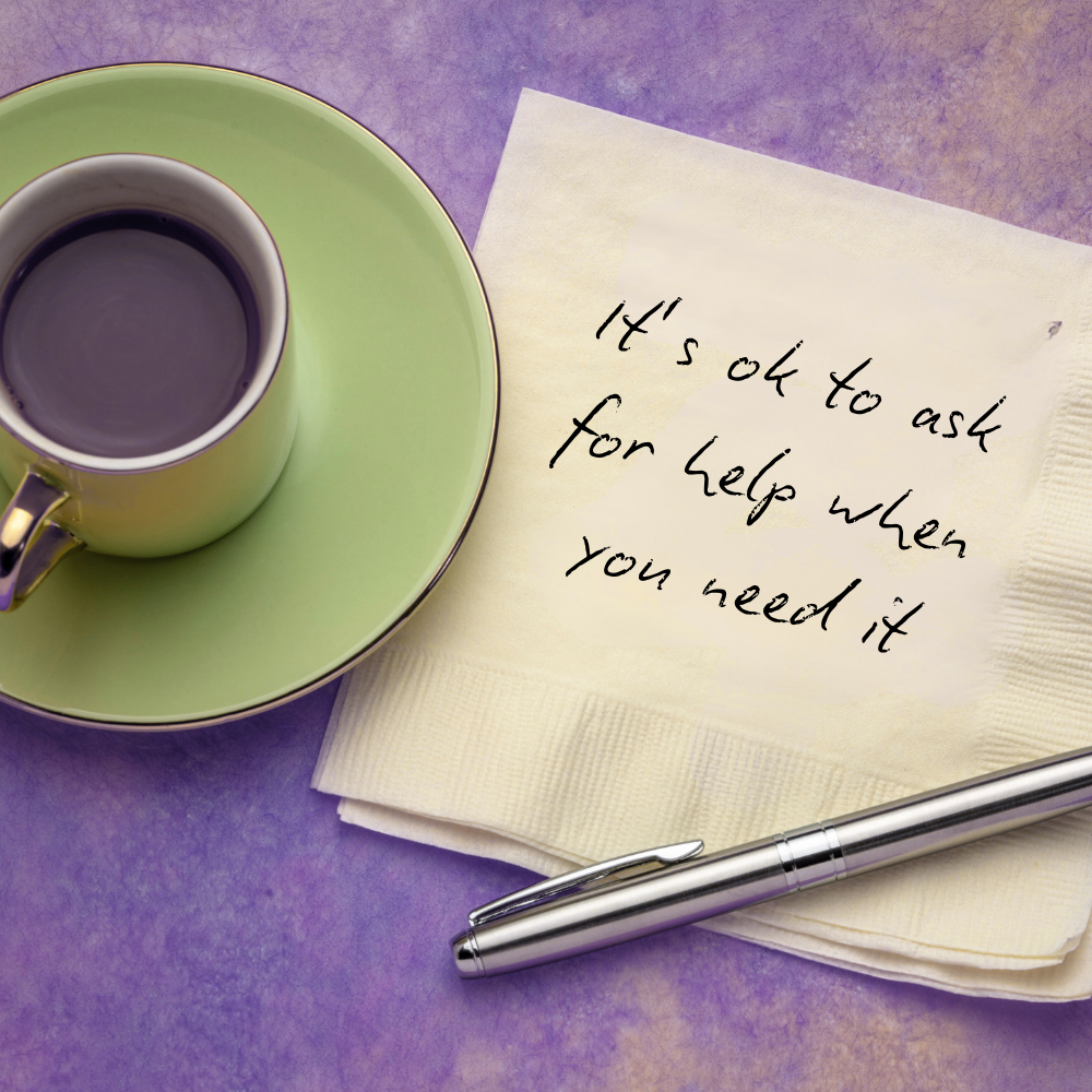 A small cup of black coffee on a green saucer, resting on a purple surface. Next to it is a handwritten note on a napkin that says, 'It's ok to ask for help when you need it,' and a silver pen.