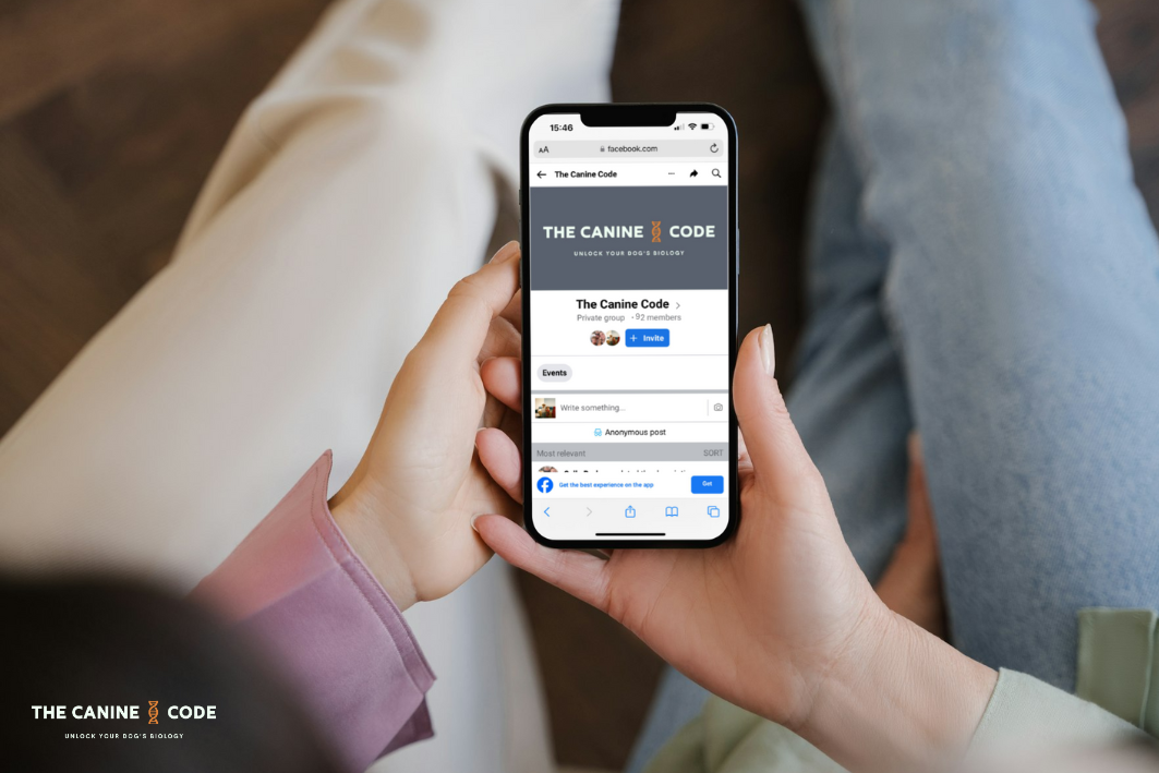 Person holding a smartphone displaying a Facebook group called 'The Canine Code' with a logo and group description.