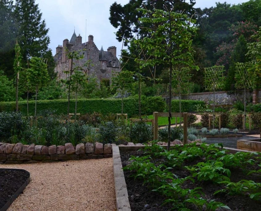 A view of the Kilcoy Castle from the Marian Garden, showing borders, paths, walls, trees, a lawn and hedging.