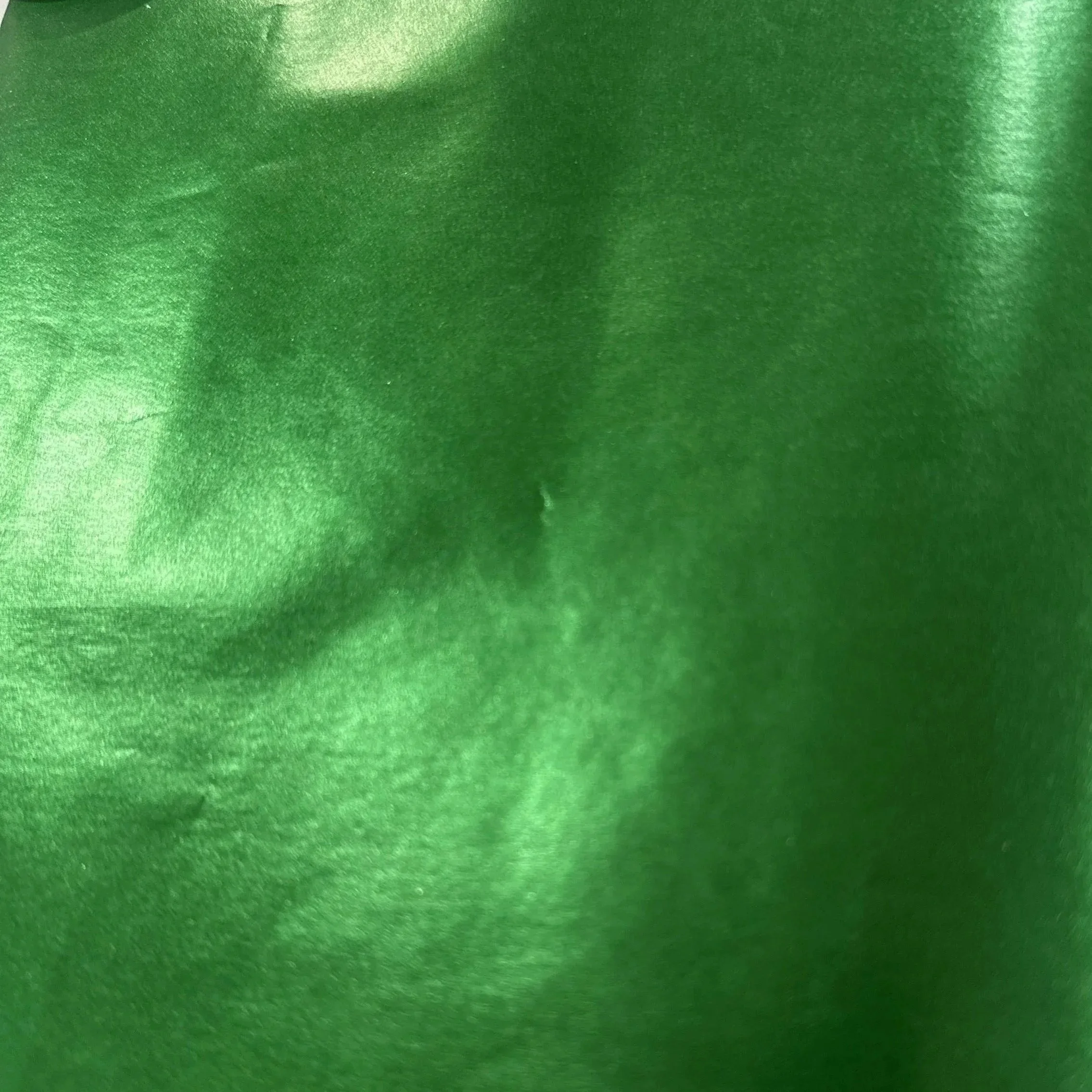 Close-up of shiny green satin fabric with smooth texture and slight wrinkles.