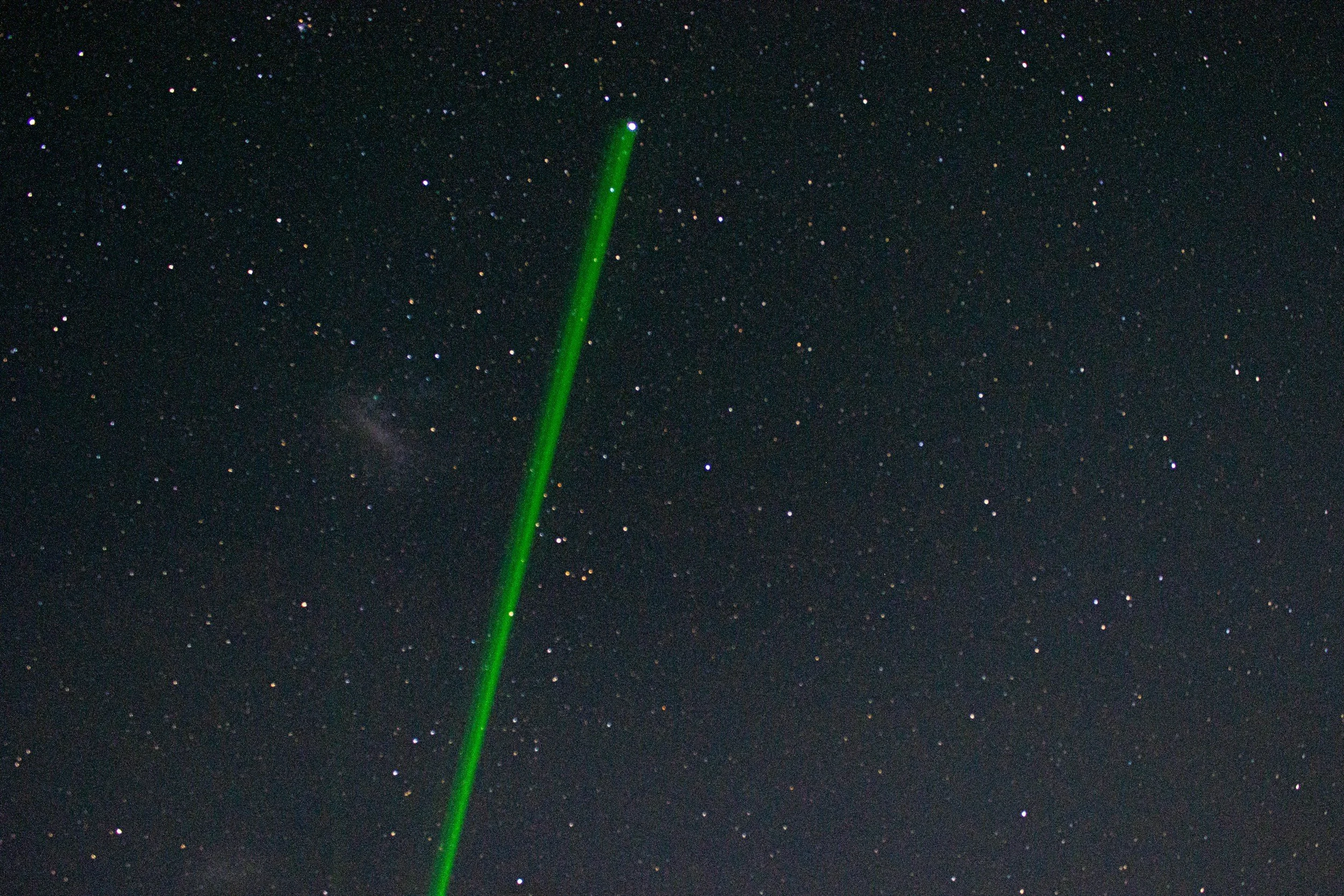 A green laser beam pointing upwards against a starry night sky with numerous small stars.