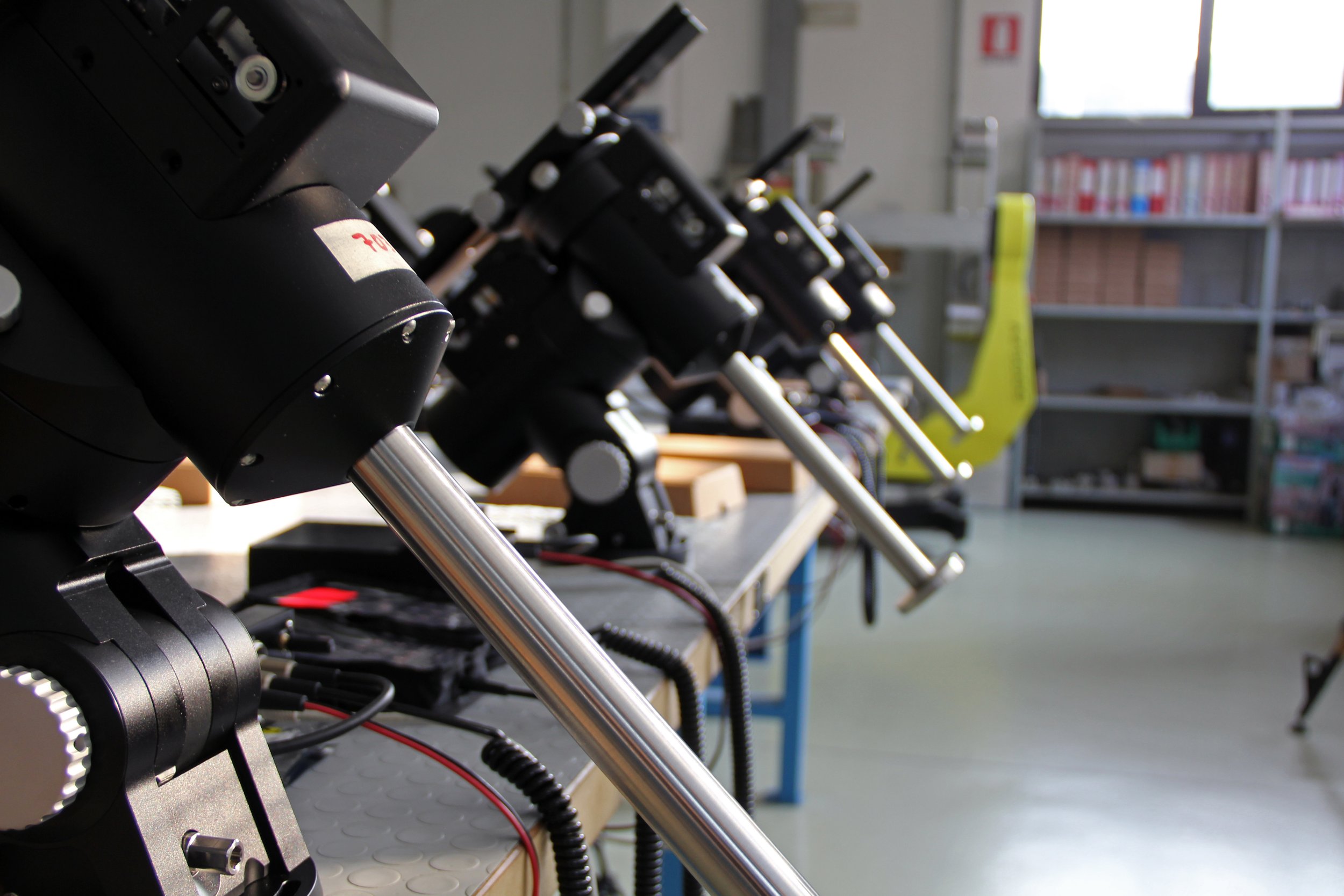 A row of black mounts lined up on a workbench in a laboratory or workshop setting, with shelves and tools in the background.