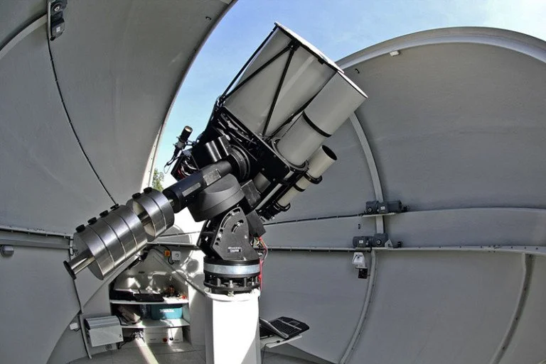 A large telescope inside an observatory with the observatory's curved roof open to the sky.