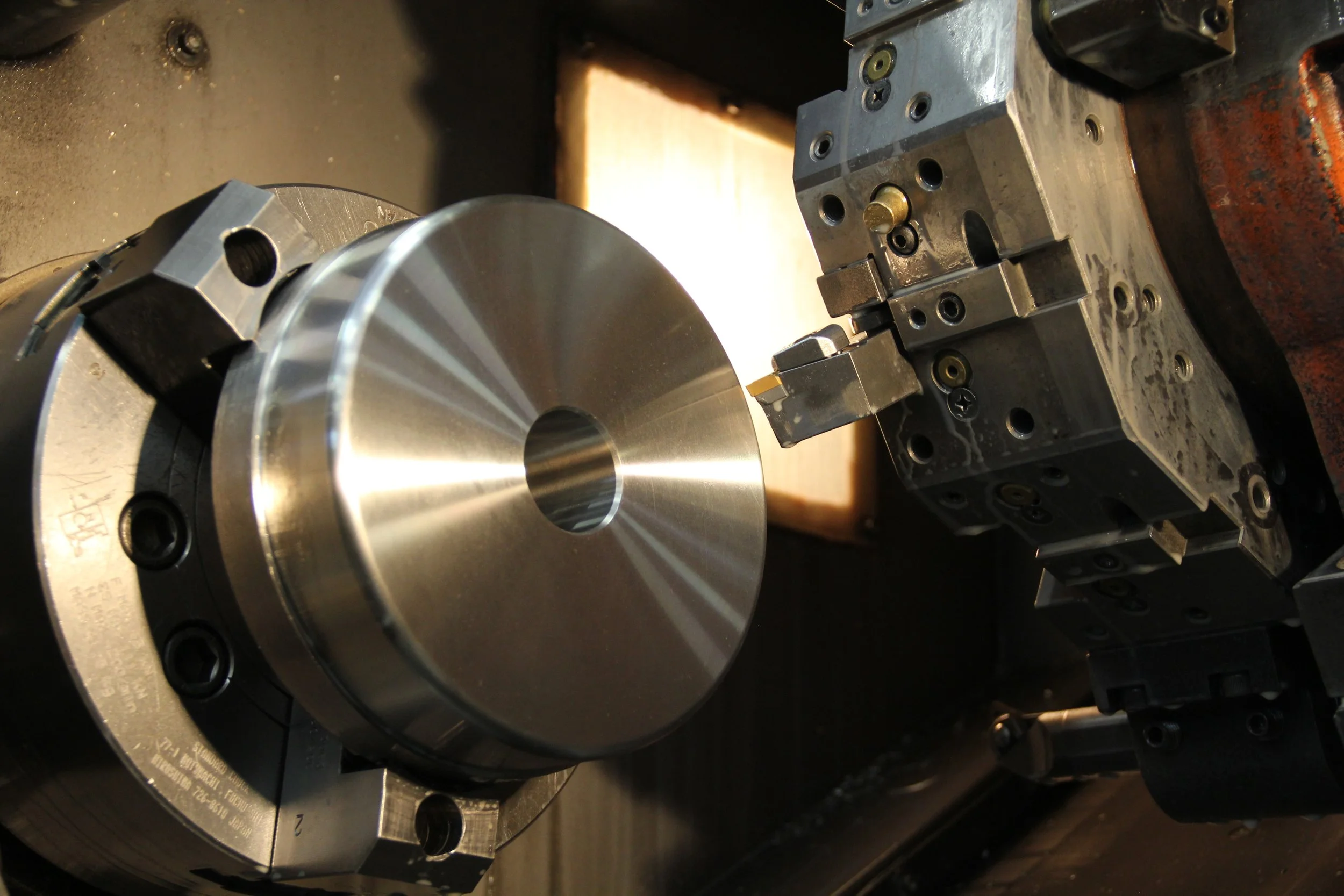 Close-up of a metal workpiece being machined by a CNC lathe machine in a workshop.