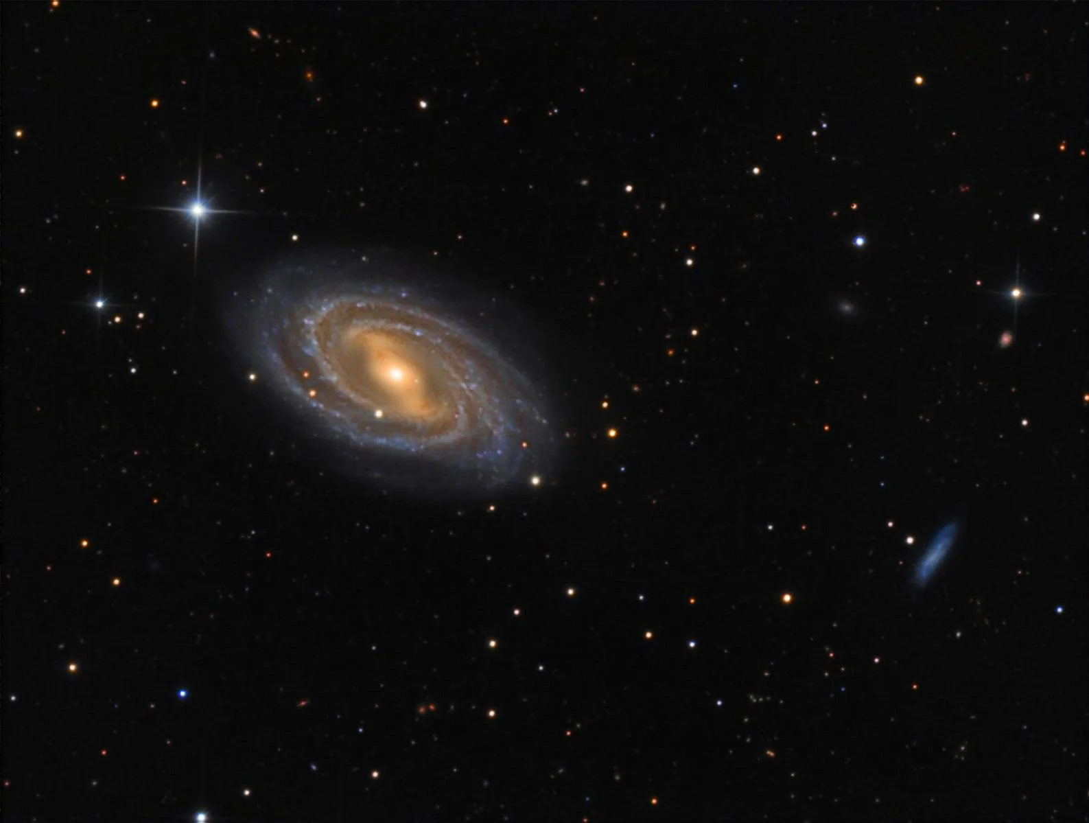 An image of a spiral galaxy with a bright core, surrounded by blue and orange arms, set against a backdrop of numerous stars and distant galaxies in space.