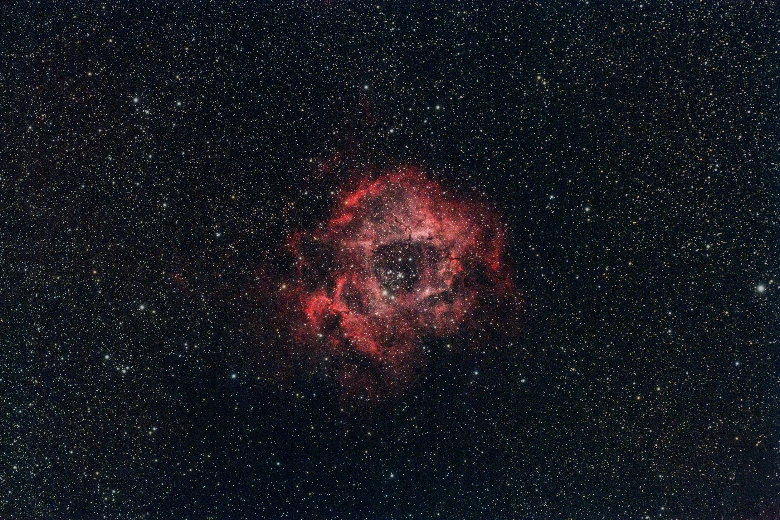 A colorful nebula with red, pink, and purple hues surrounded by countless stars in outer space.