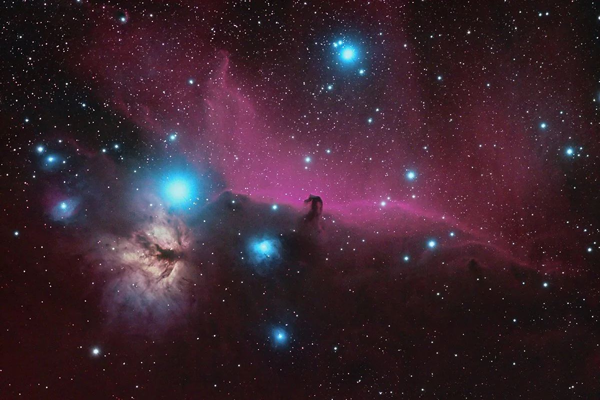 A colorful deep space photograph depicting a nebula with bright blue and purple hues, surrounded by numerous stars of varying sizes and brightness.