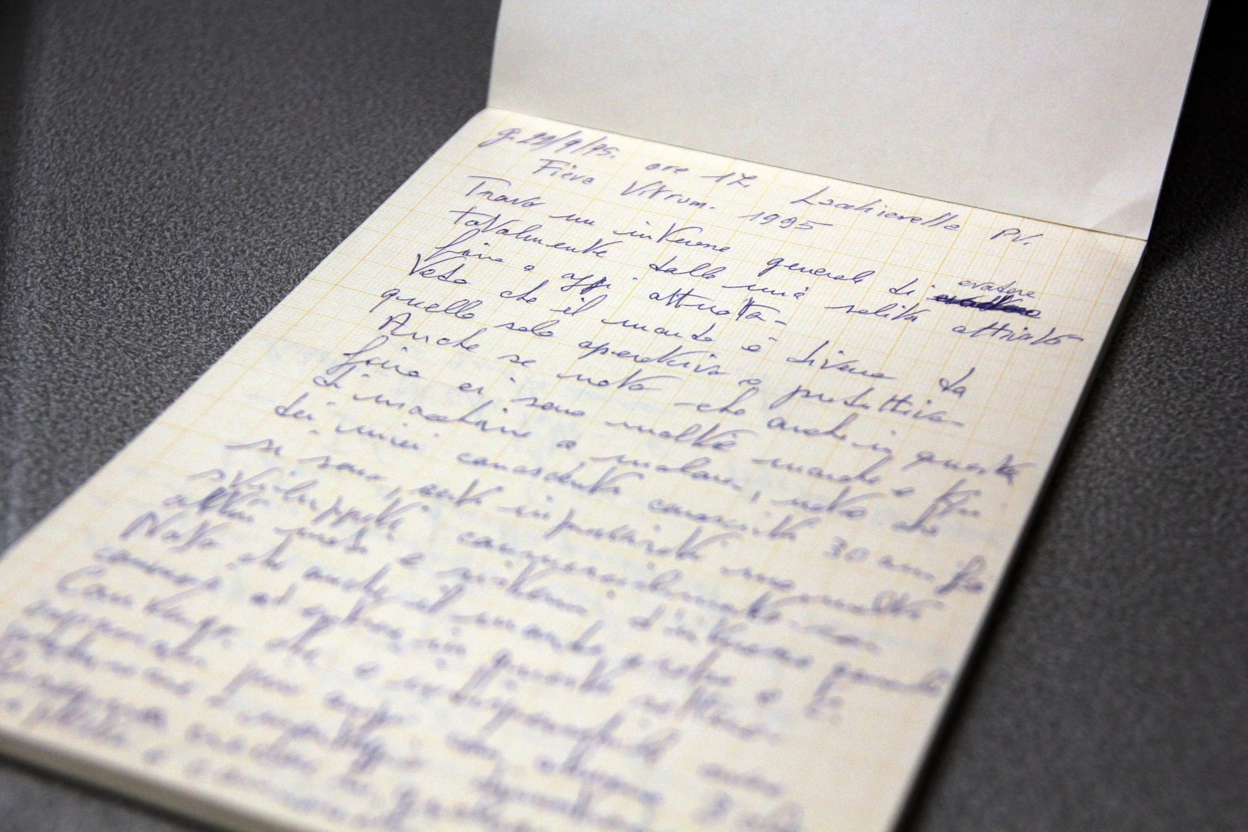 A handwritten letter in Italian on graph paper in an open notebook, laying on a dark surface.