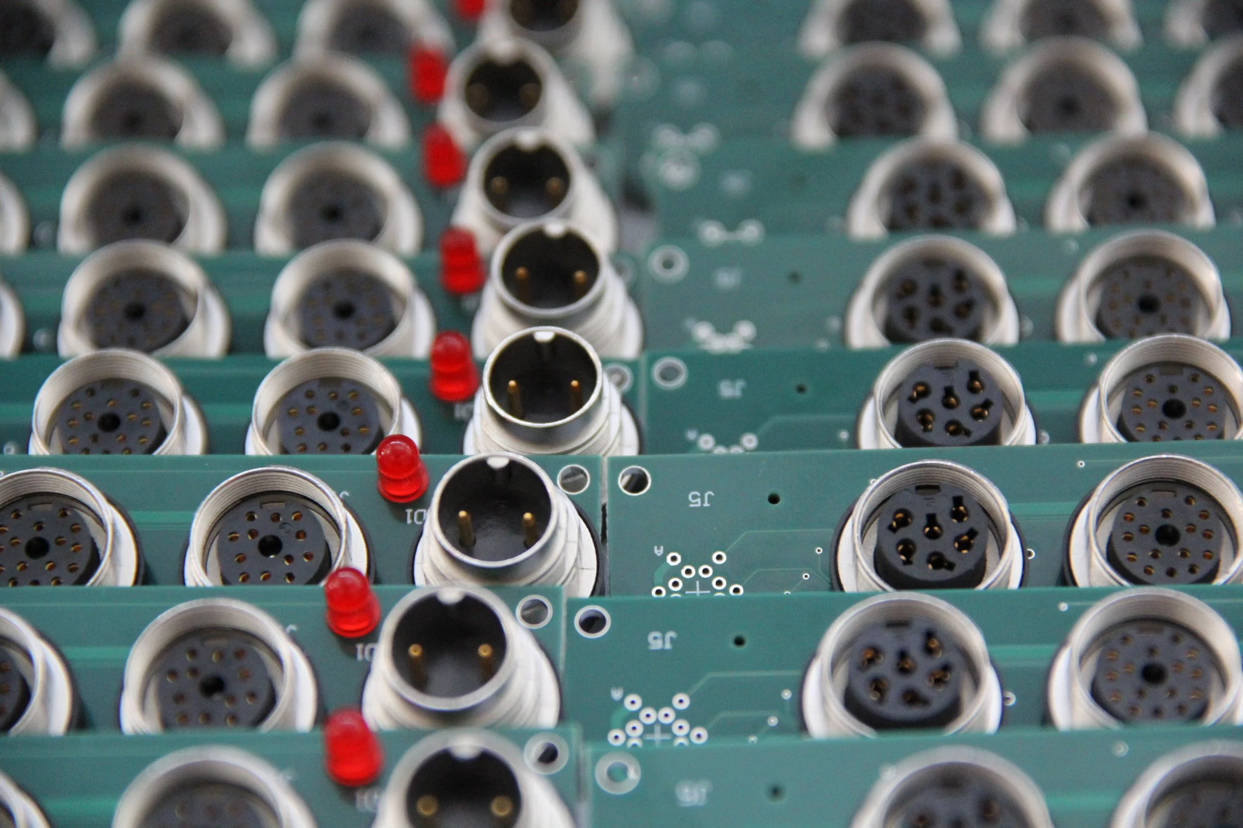 Multiple circular electronic connectors mounted on green circuit boards, with some red indicator lights.