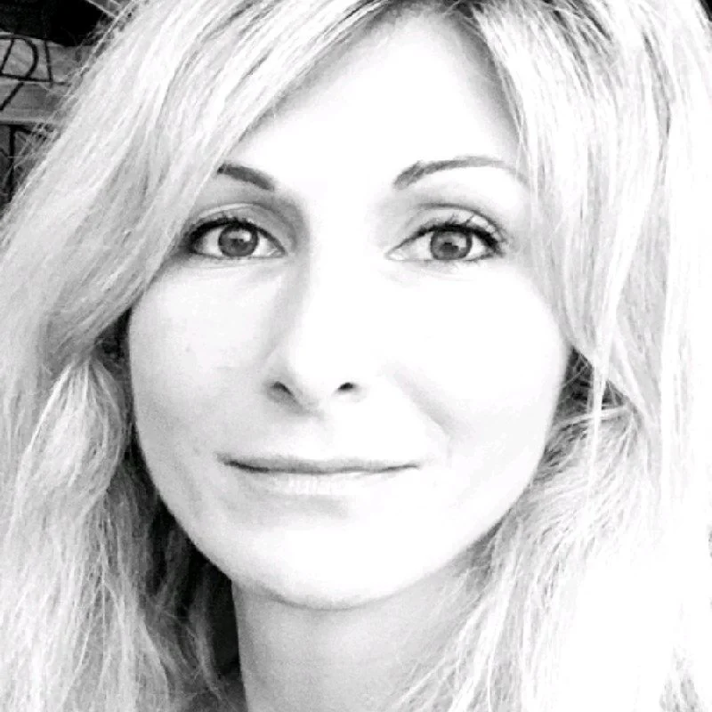 Schwarz-weiß-Foto einer lachenden Frau mit langen, gewellten Haaren und hellem Teint, Blick direkt in die Kamera.