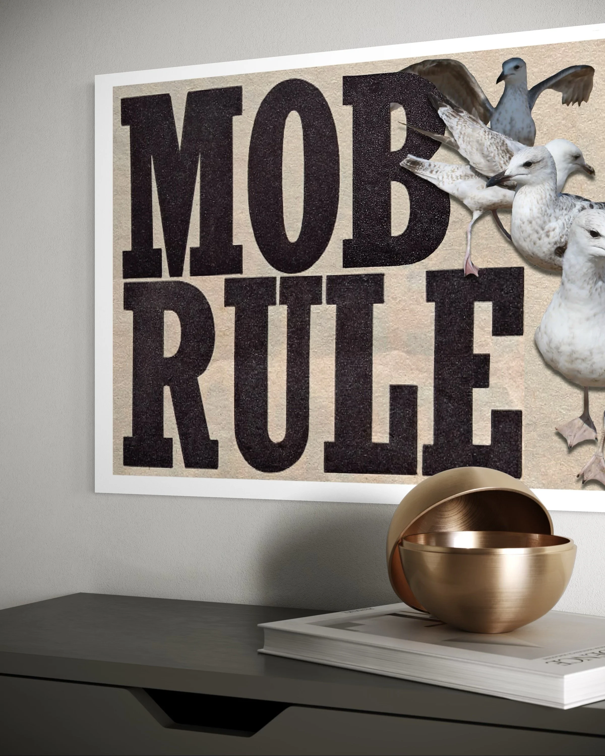 Decorative poster with the bold text 'MOB RULE' on the wall, featuring a cluster of seagulls flying nearby, and a metallic bowl and magazine on a gray surface below.