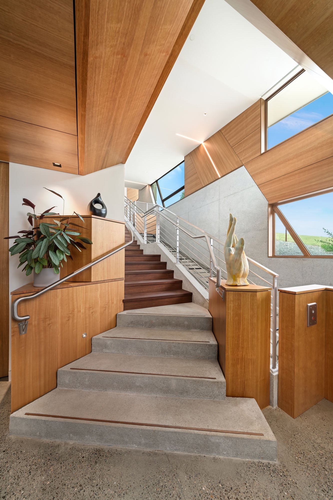 Modern stairway interior with wood paneling, concrete steps, large windows, and decorative sculpture.