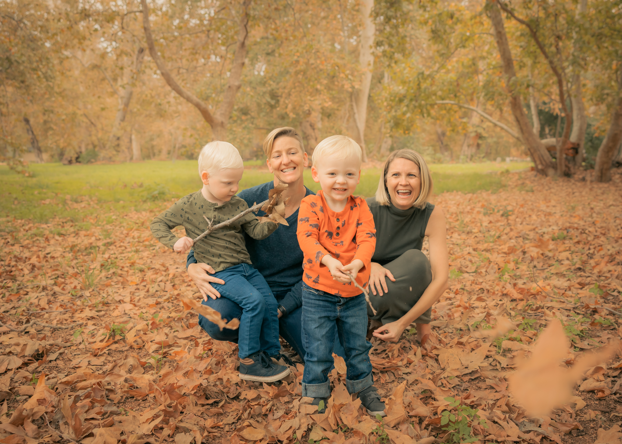 Two women and two young boys playing in a park with autumn leaves and trees in the background.
