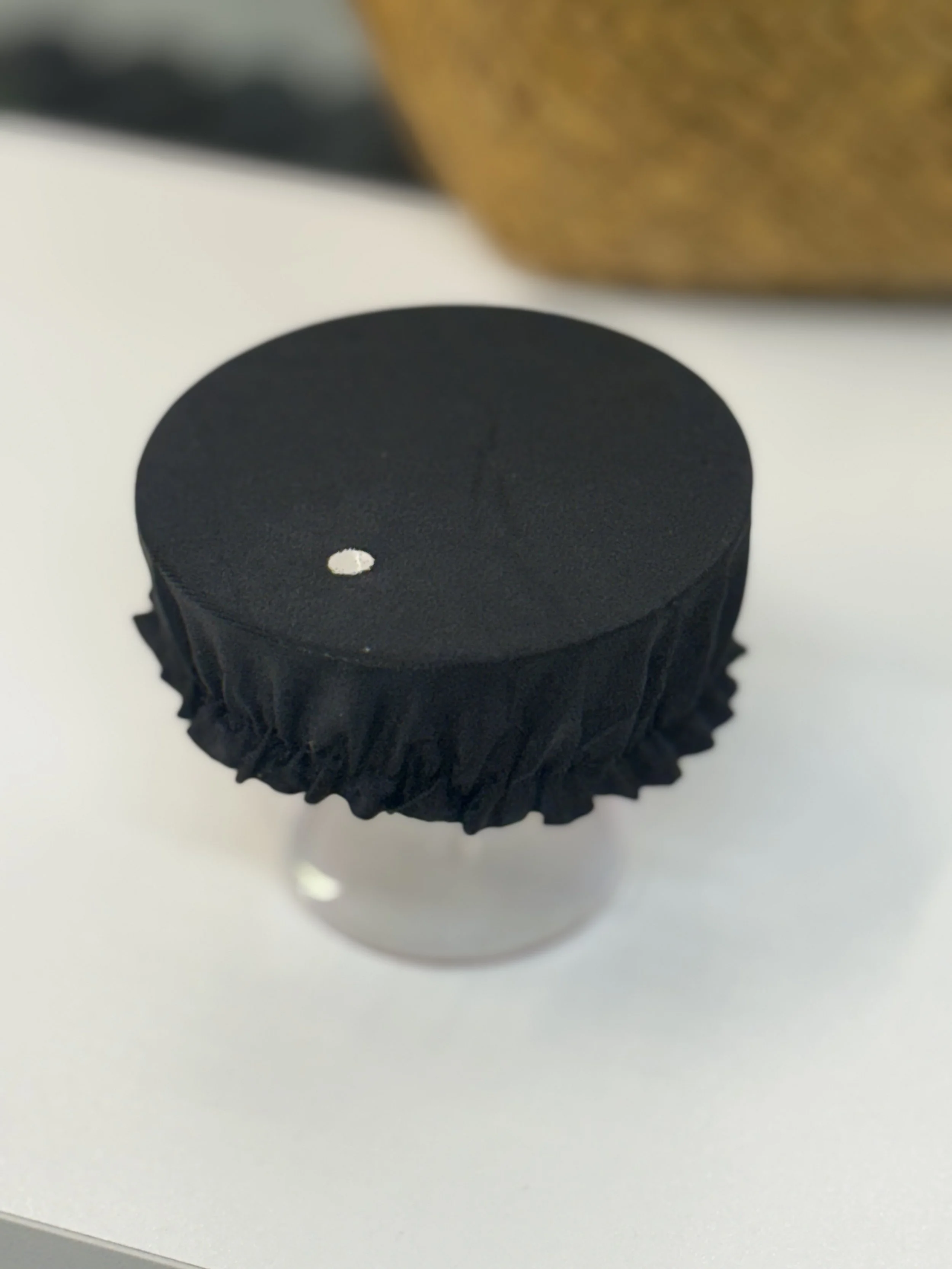 Close-up of a black bottle cap on top of a white container, with a small white dot on the cap.