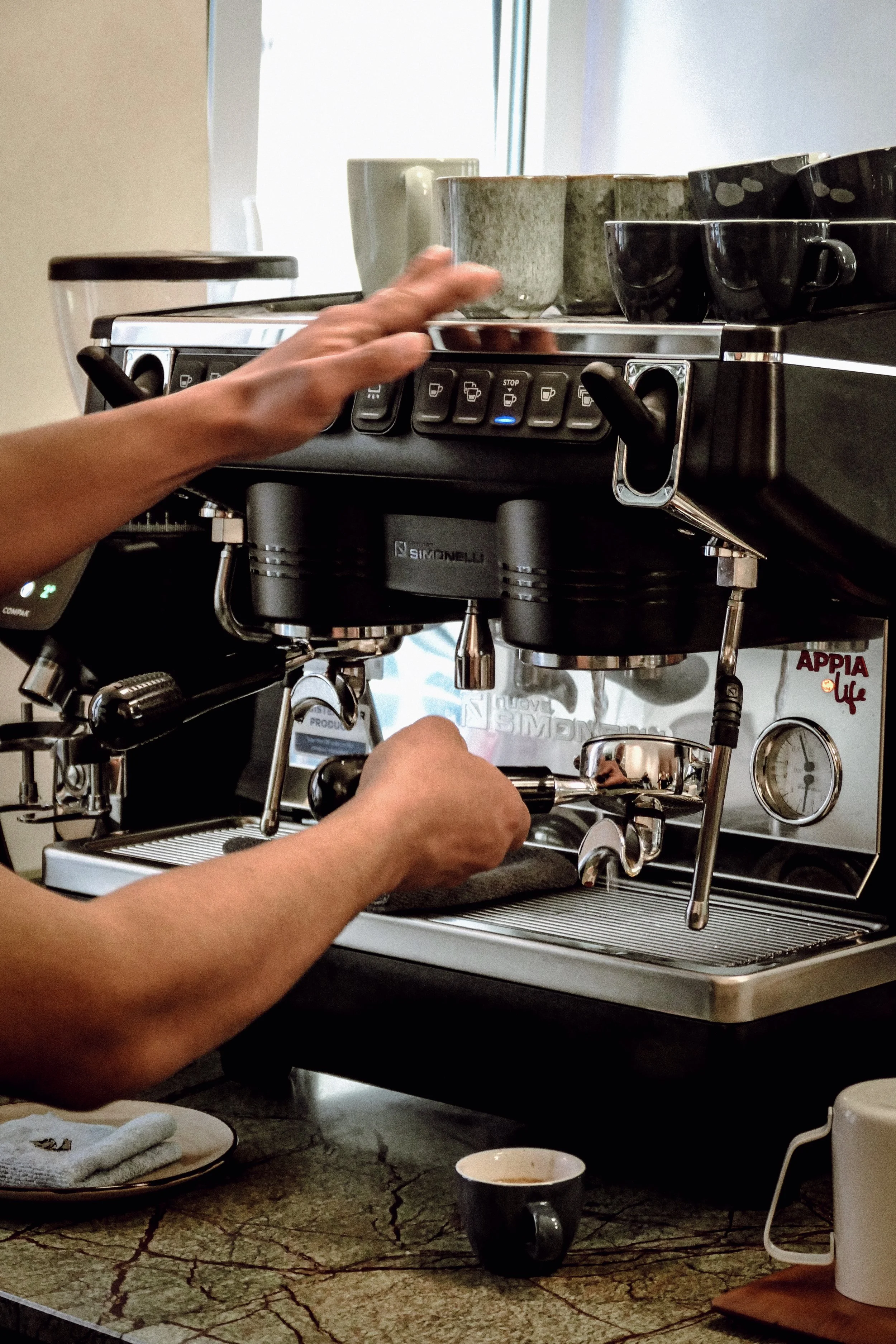 Close-up of a barista preparing espresso with a professional espresso machine, several cups on top, and a small cup of coffee in front.