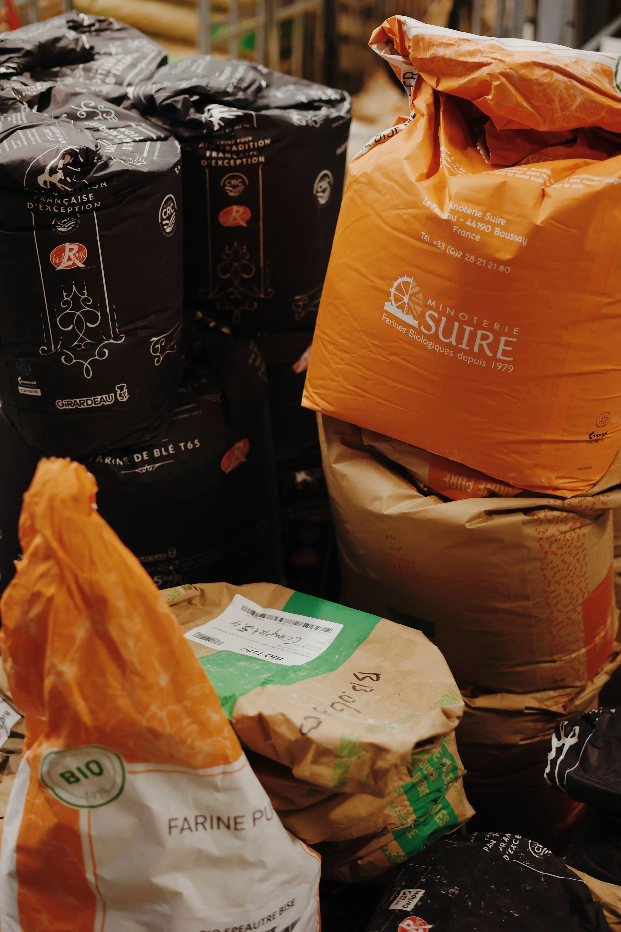 Bags of flour and grains stacked together in various colors including orange, black, and beige.