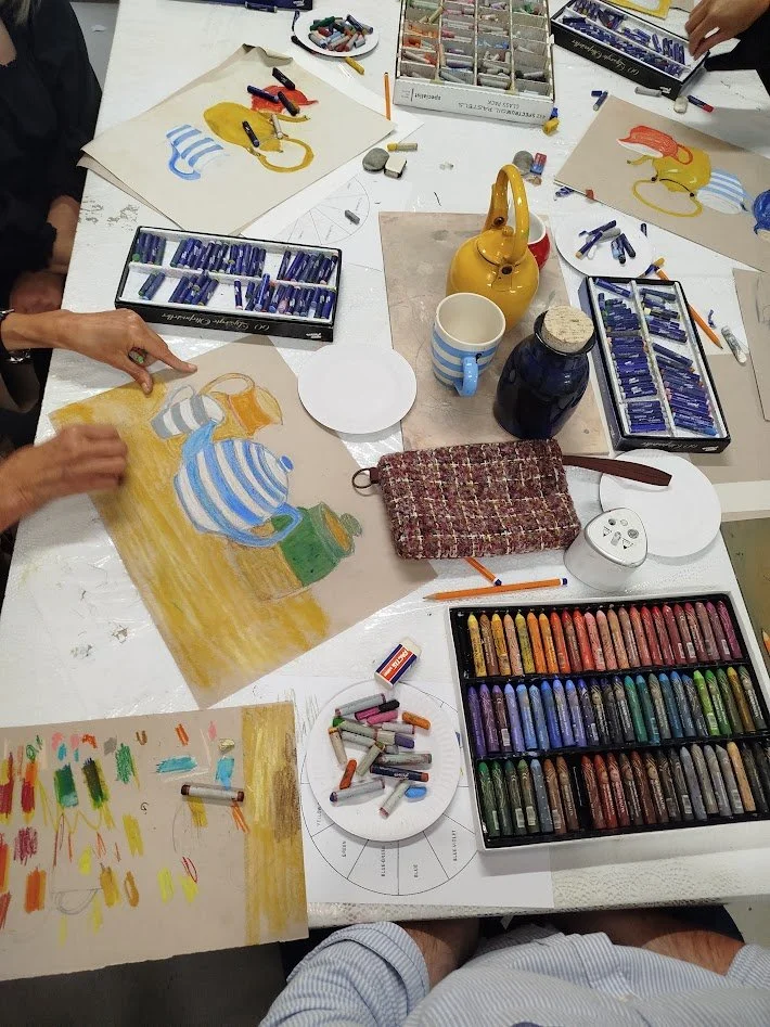 a depiction of a table set up for an art class, with hands working on a drawing
