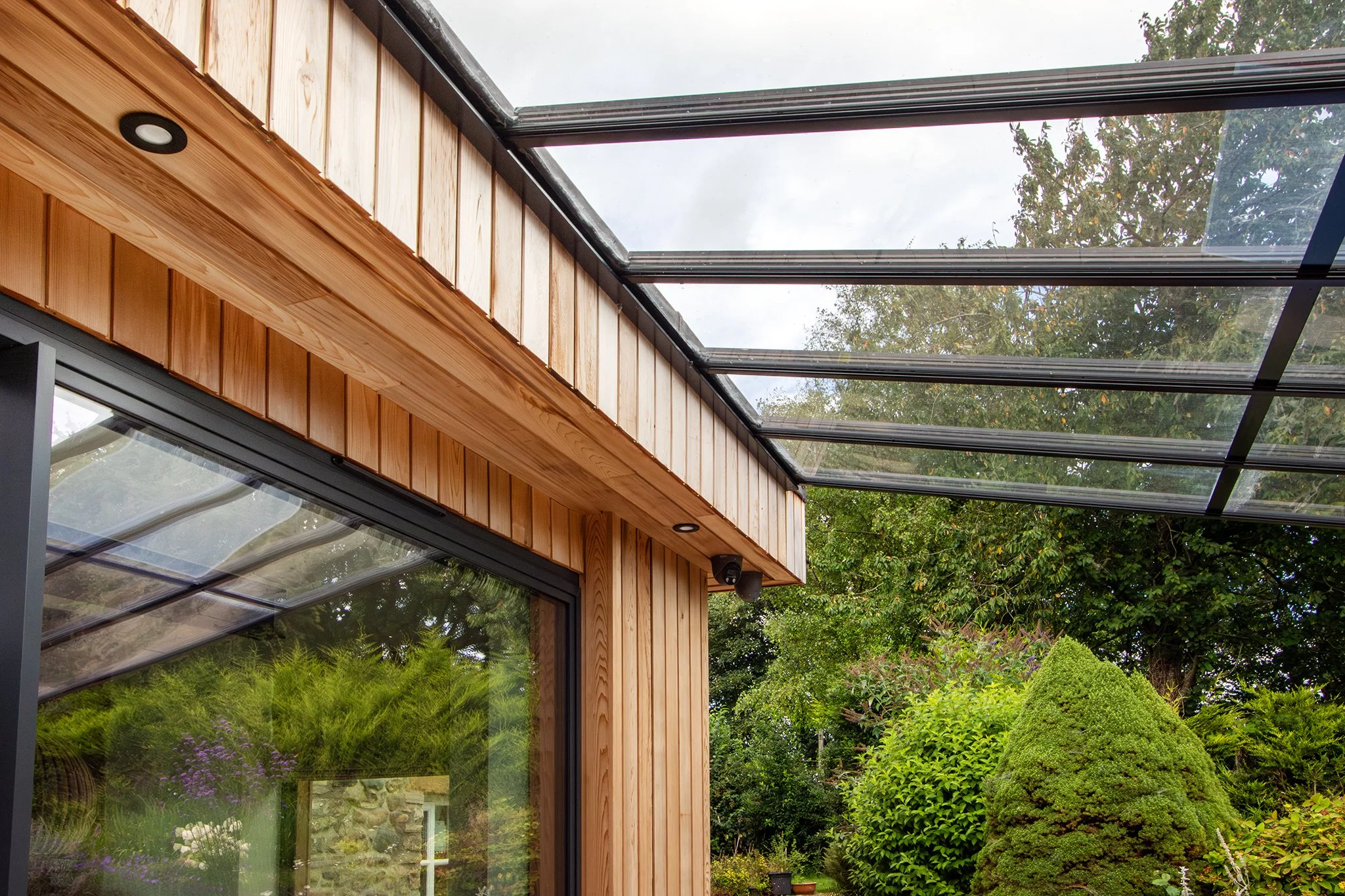 A modern house with large glass windows and a glass ceiling, surrounded by green trees and bushes.
