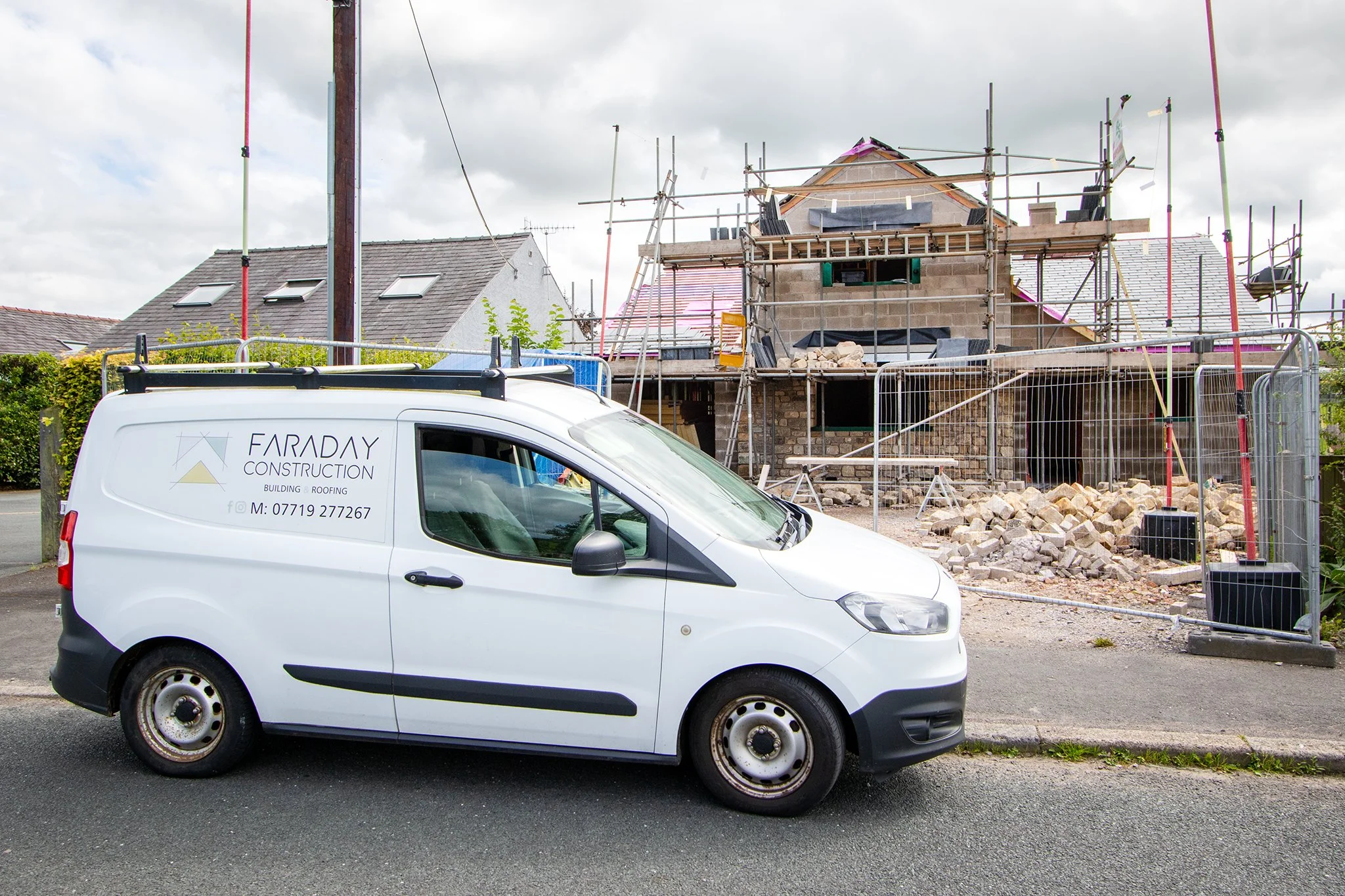 Construction site with a house under construction, scaffolding around it, and a white contractor's van parked in front.