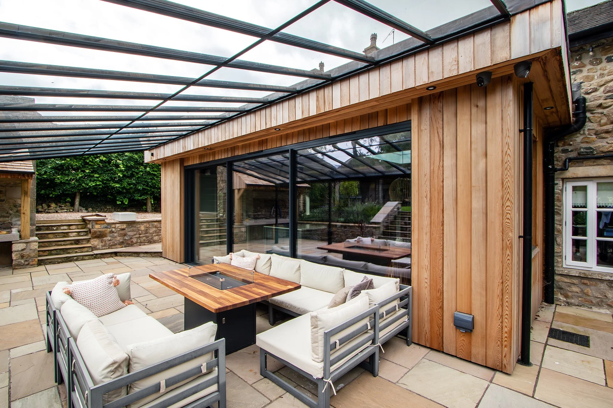Outdoor patio with seating area, wooden walls, glass roof, and stone patio floor