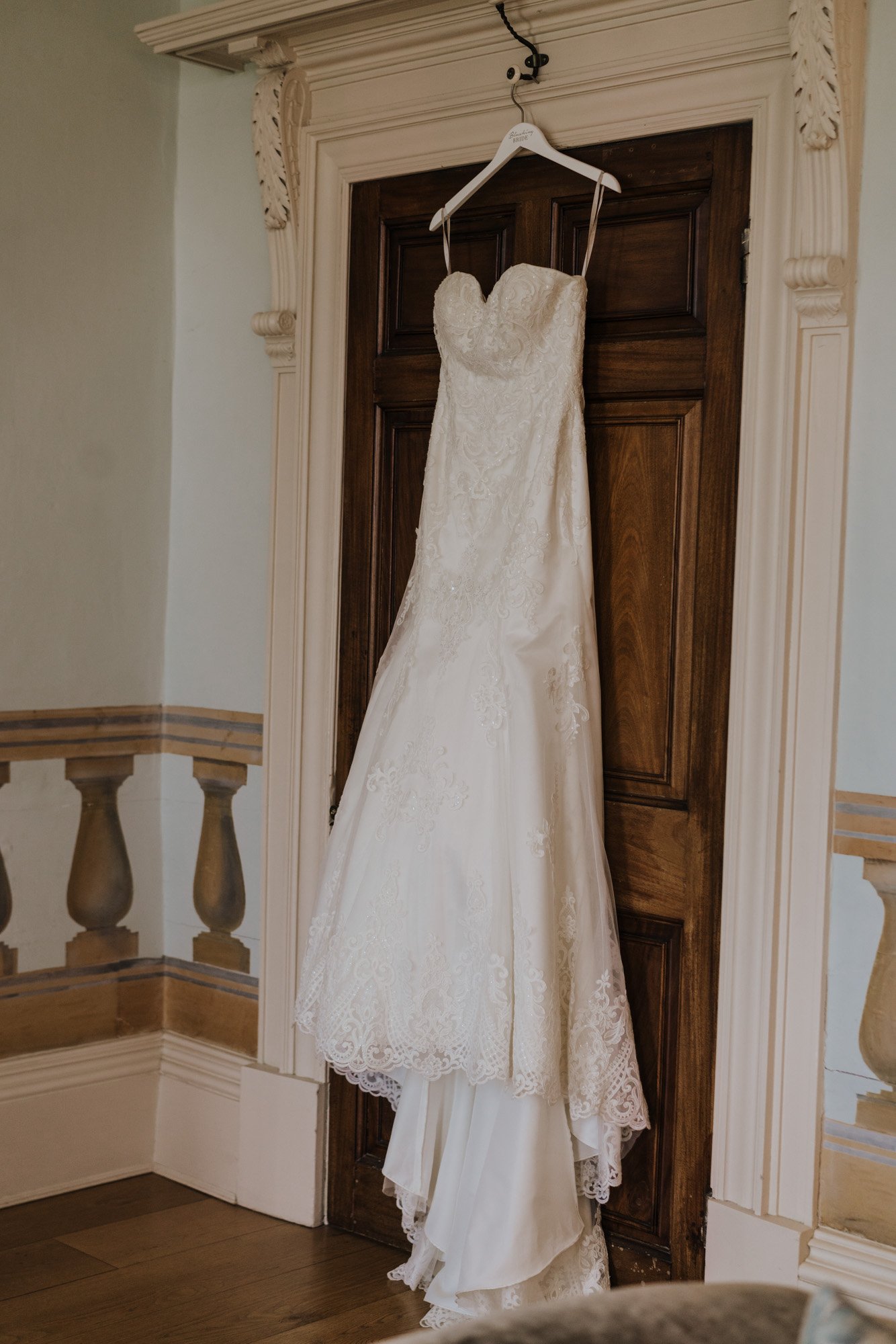 A wedding dress hanging on a hanger off a door with ornate white trim.
