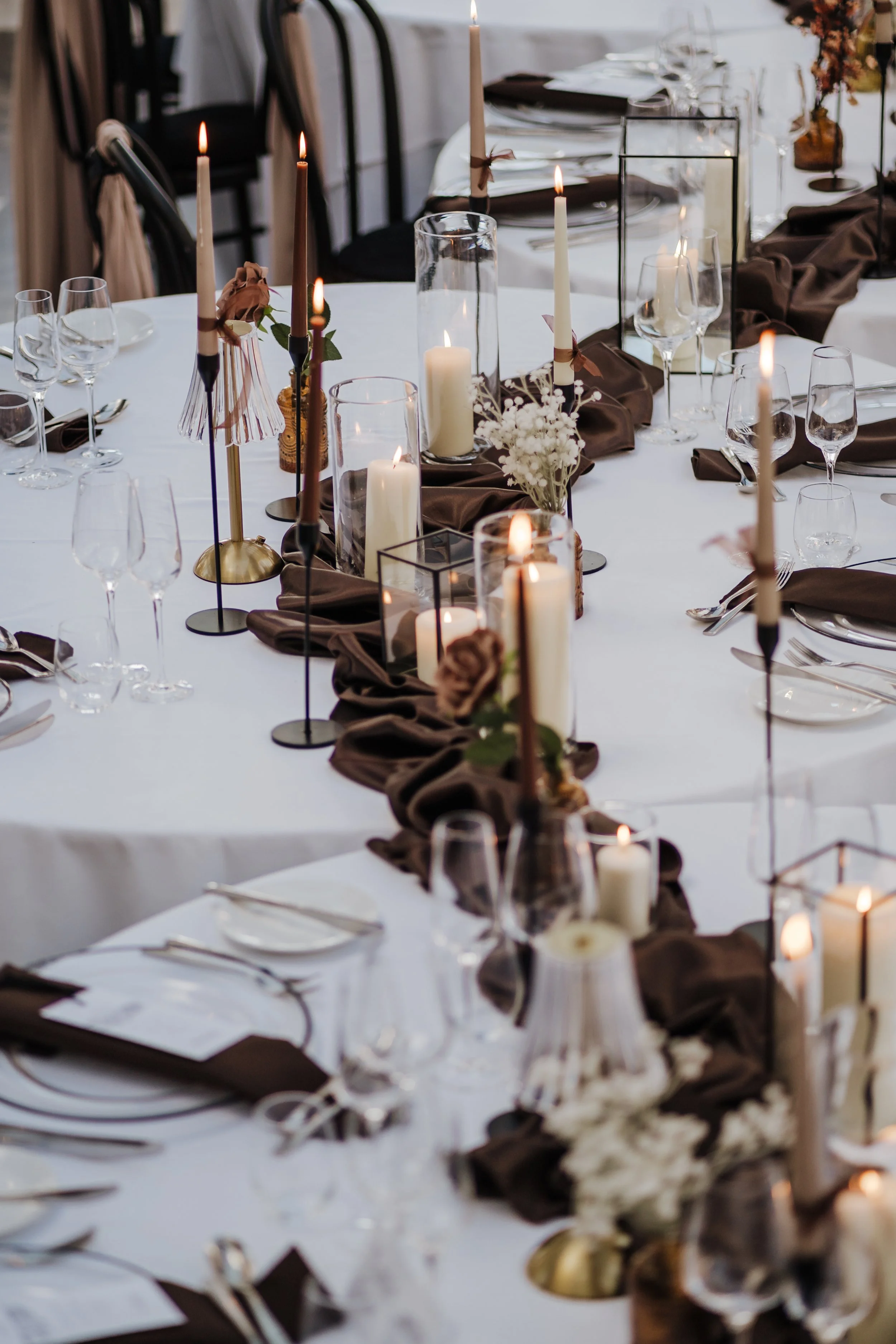 Elegant dining table decorated with candles, floral arrangements, and dark brown napkins for a formal event.