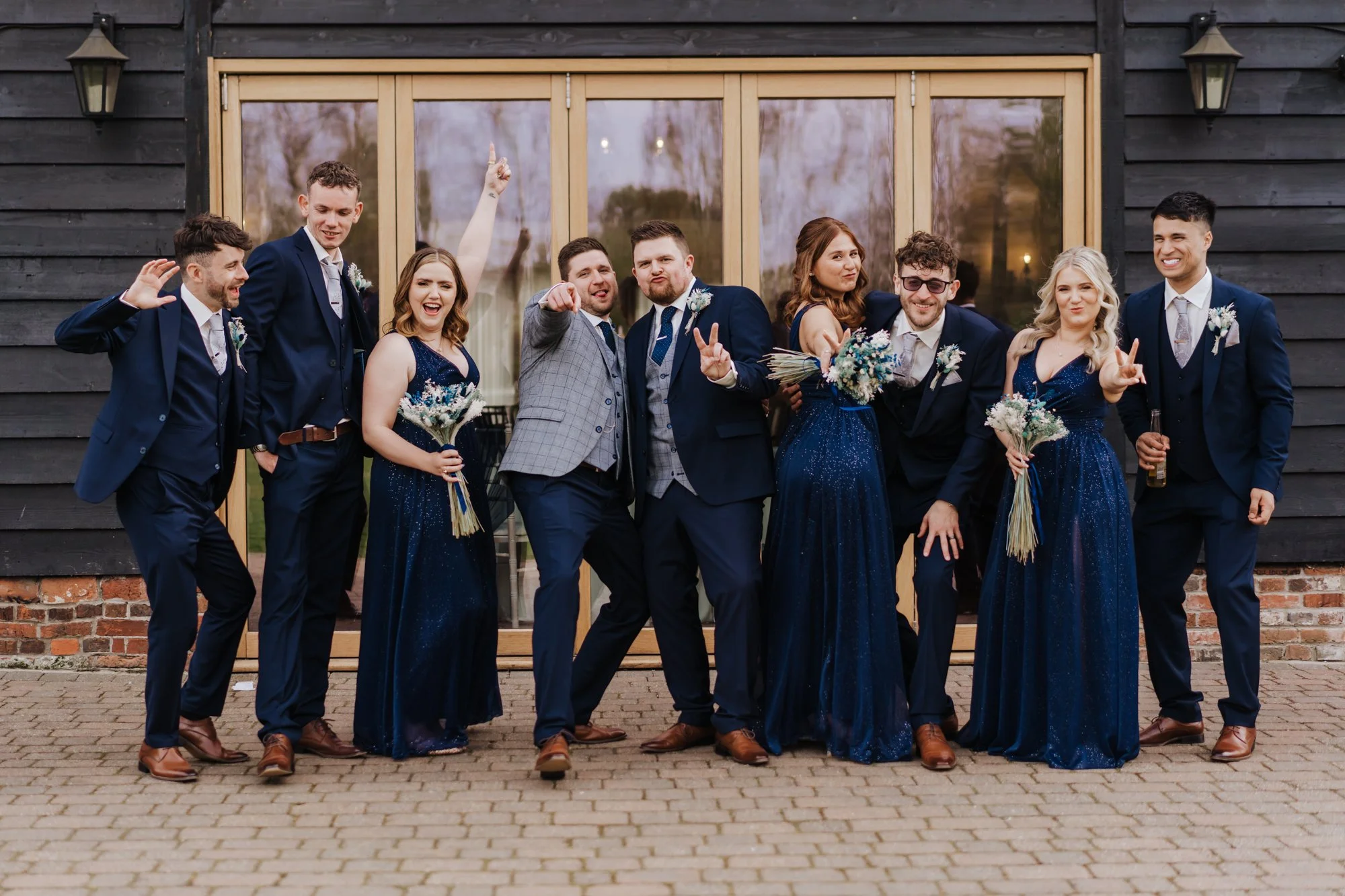 A group of ten people dressed in formal attire, posing and celebrating outside a building with sliding glass doors, during what appears to be a wedding or special event.