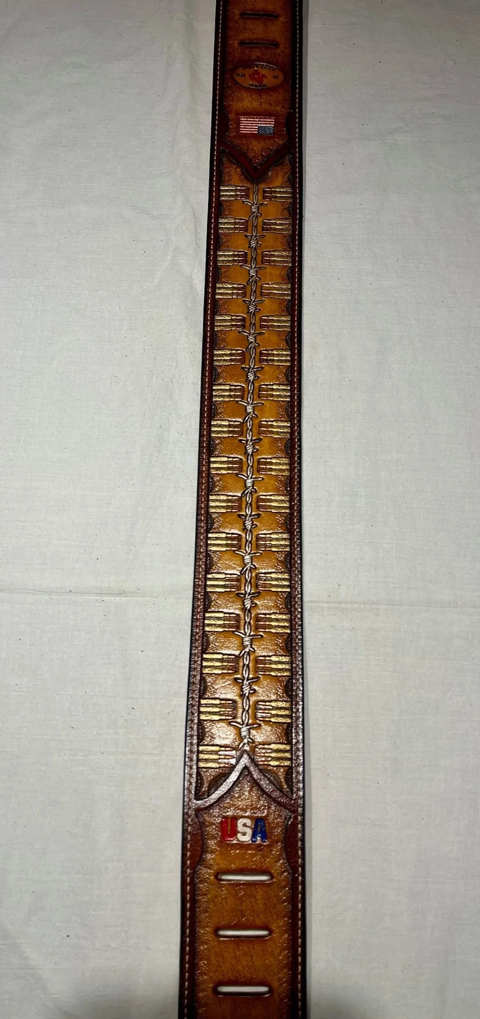 A long brown leather belt with military and patriotic patches, including an American flag and a U.S.A. emblem, laid flat on a white surface.