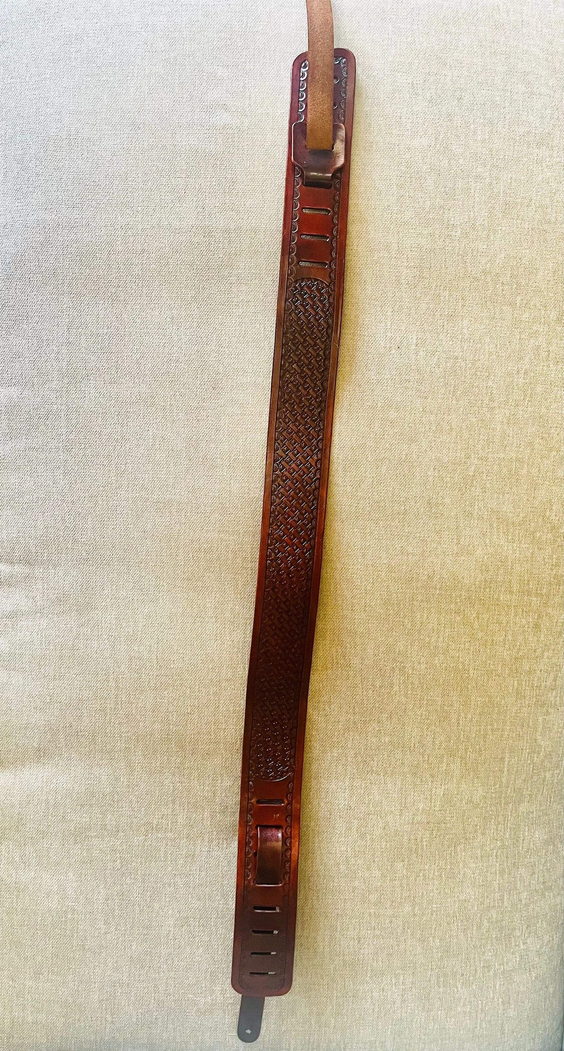 A brown leather watch strap with a textured pattern, attached to a metal buckle, hanging vertically against a beige fabric background.