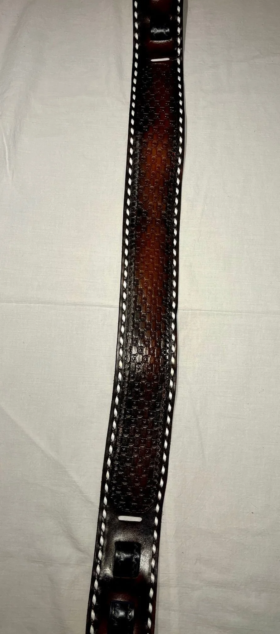 A leather belt with white stitching laid flat on a light-colored surface.
