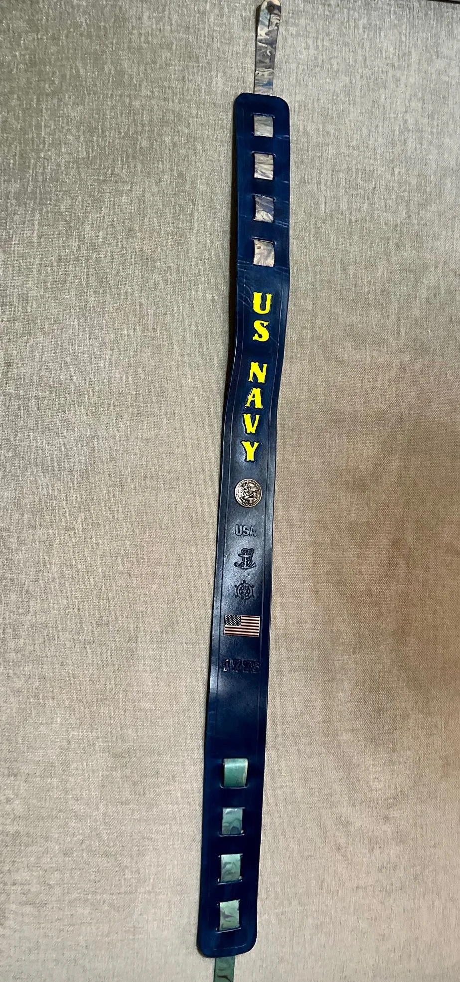 A military ID bracelet with the words 'US NAVY' in yellow letters, military insignia, and an American flag.