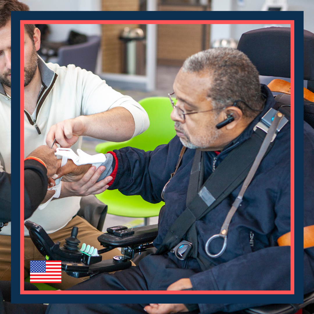 A man in a wheelchair with a headset receiving medical assistance from another man.
