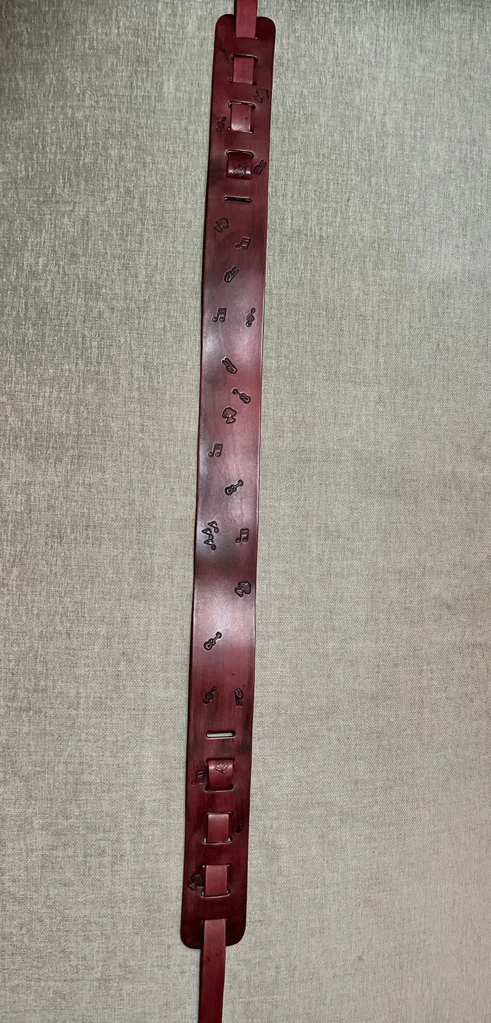 Red strap with musical symbols and phone icons attached, hanging vertically against a light fabric background.