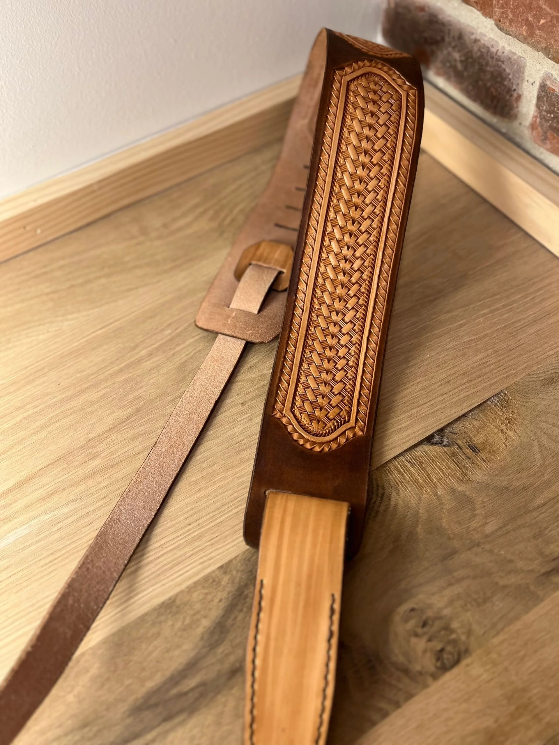 Decorative leather belt with a woven leather detail on a wooden surface.