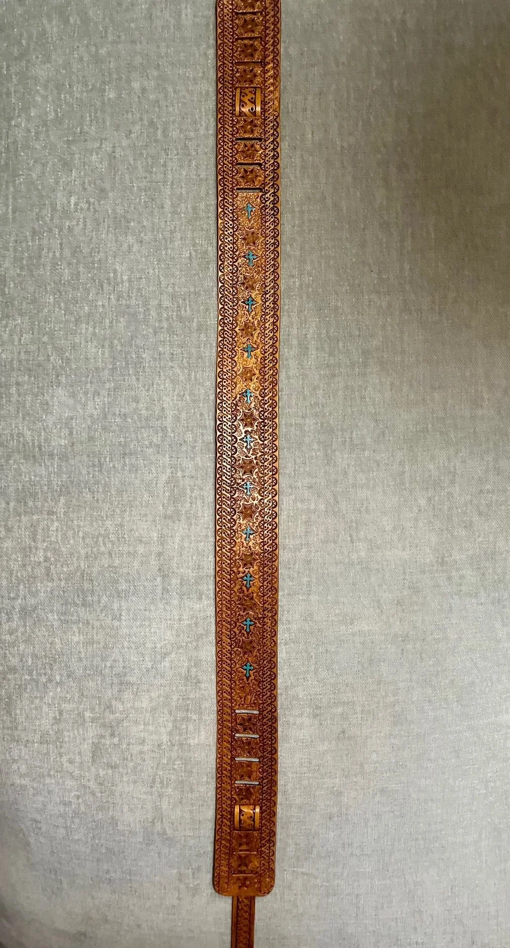 A vertical carved and decorated strip of material, possibly wood or metal, with intricate patterns including stars and crosses, mounted on a plain gray background.