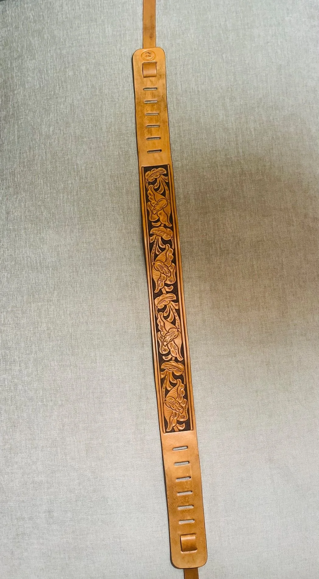 A wooden slap bracelet with carved floral designs, attached to a narrow wooden strip with slots.