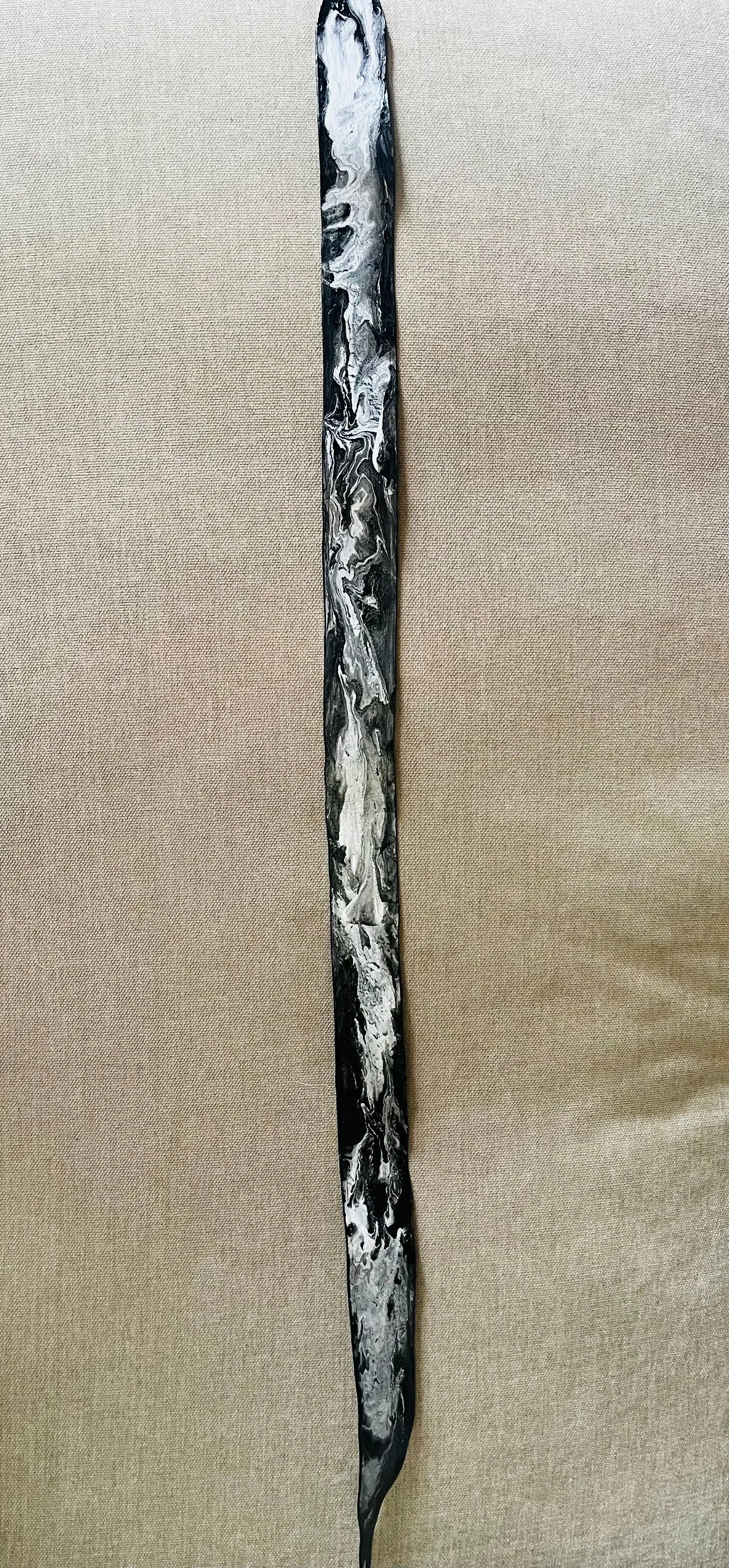 A long, narrow, abstract painting with black, white, and gray marbled patterns on a beige fabric background.