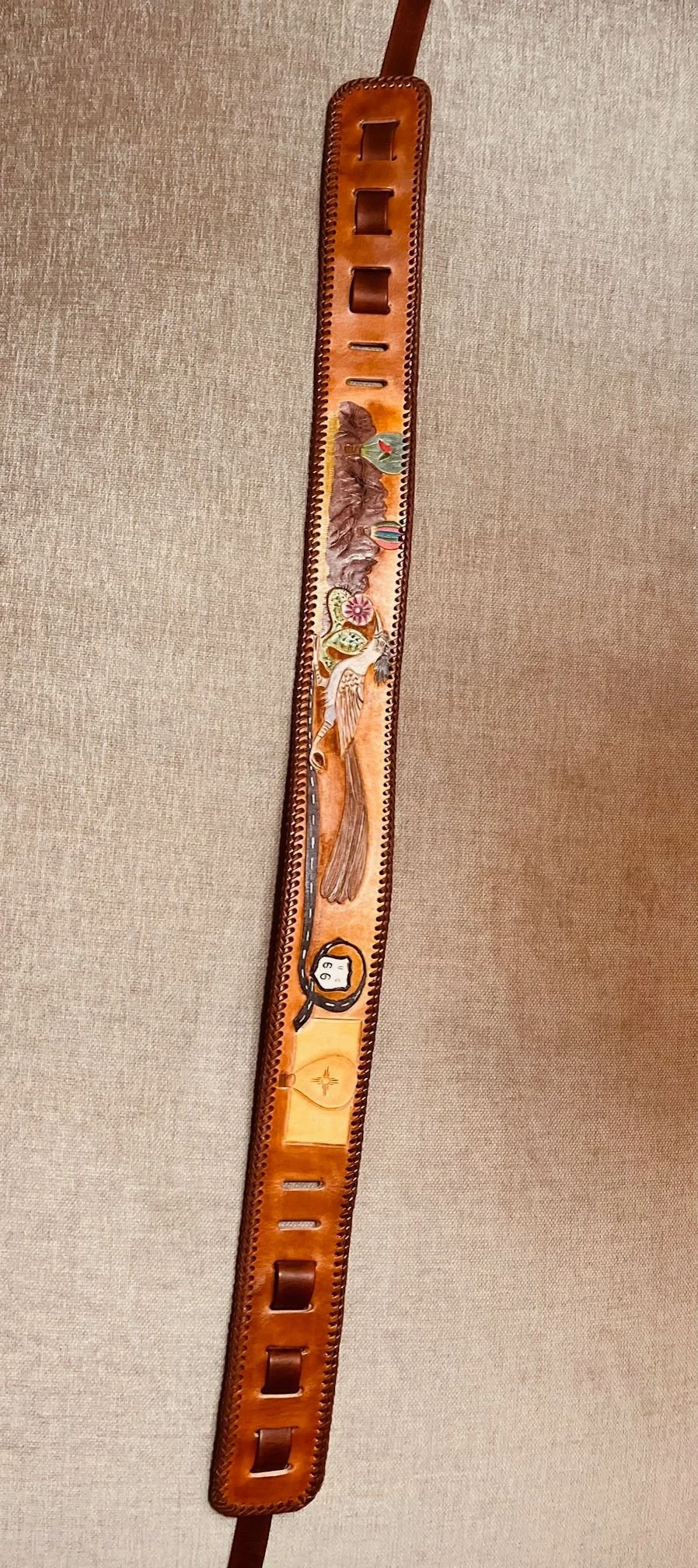 Decorative leather belt with painted desert scene, including mountains, cacti, a bird, and a sun.