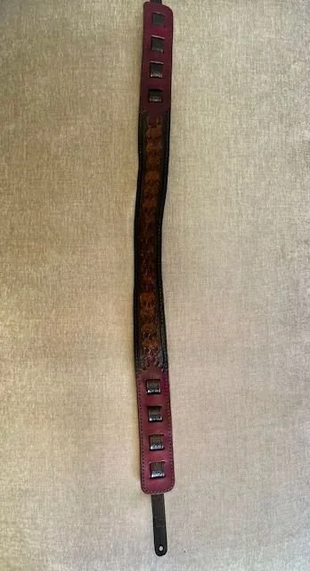 A long leather strap with multiple rectangular holes, two metal buckles, and a black end tab.