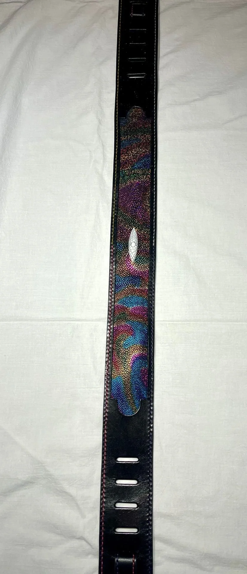 A black belt with a colorful, holographic design along the middle, placed on a white fabric background.
