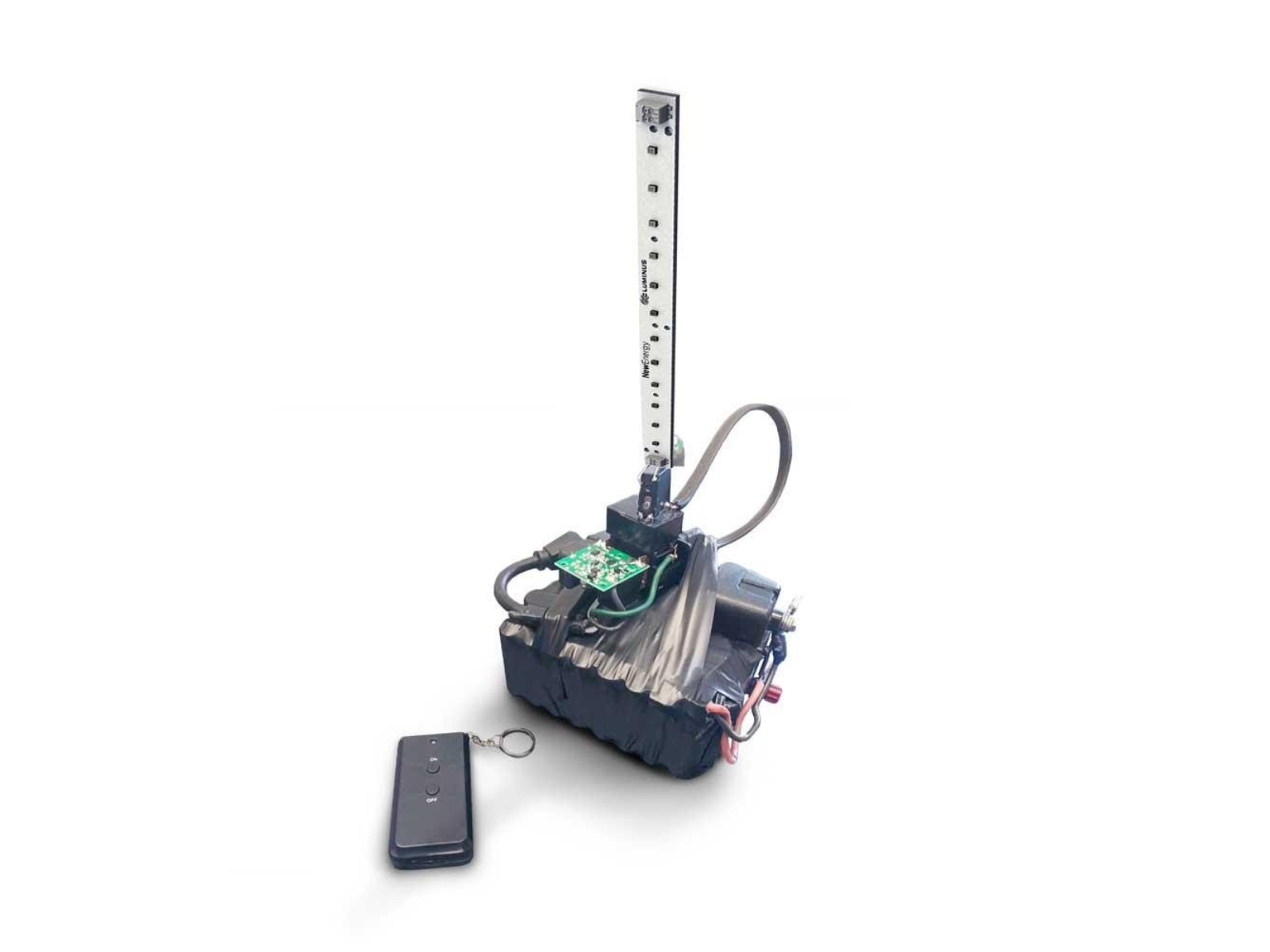 A robotic device with a vertical metal strip marked with measurement units, connected to a green circuit board and a black base, with a remote control nearby.