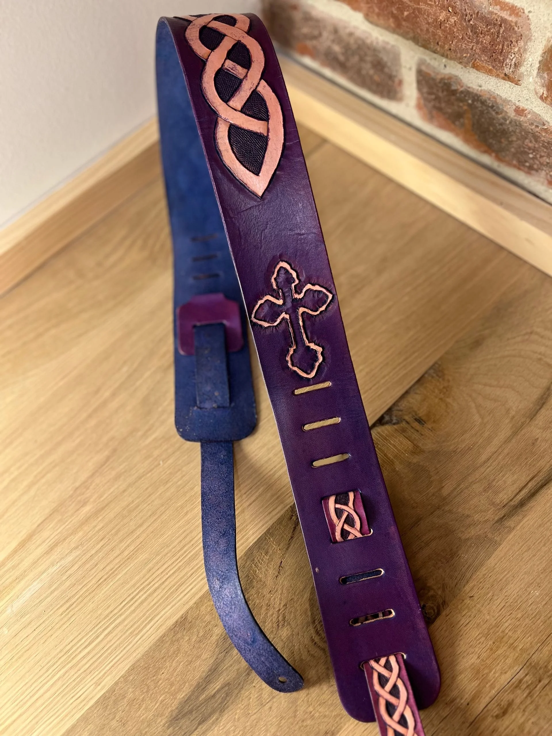 A leather bracelet with Celtic knot and cross designs etched into it, resting on a wooden surface.