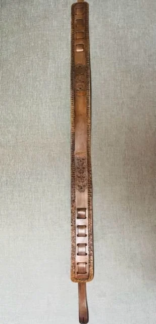 Leather guitar strap with buckles and decorative designs against a gray background.