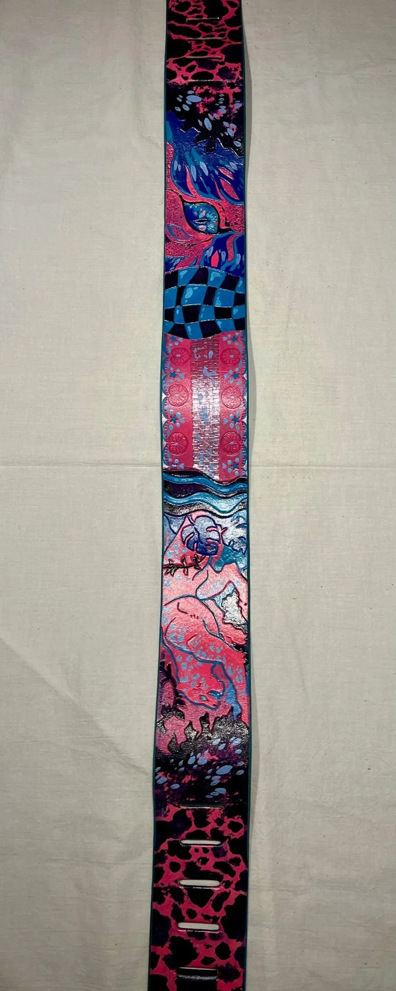 A vertical, colorful bracelet with multiple artistic segments, including abstract patterns, a checkered design, floral motifs, and a stylized flamingo at the bottom, against a beige background.