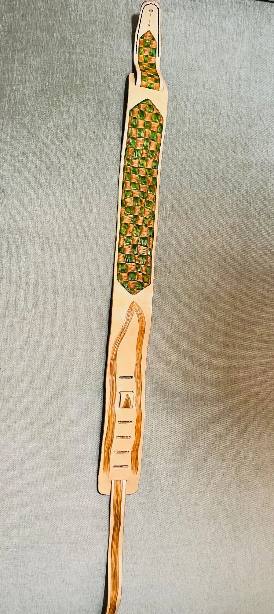 Handmade bamboo weave craft with a long, narrow paddle shape, decorated with colorful woven patterns in green, orange, and yellow hues, mounted on a plain background.
