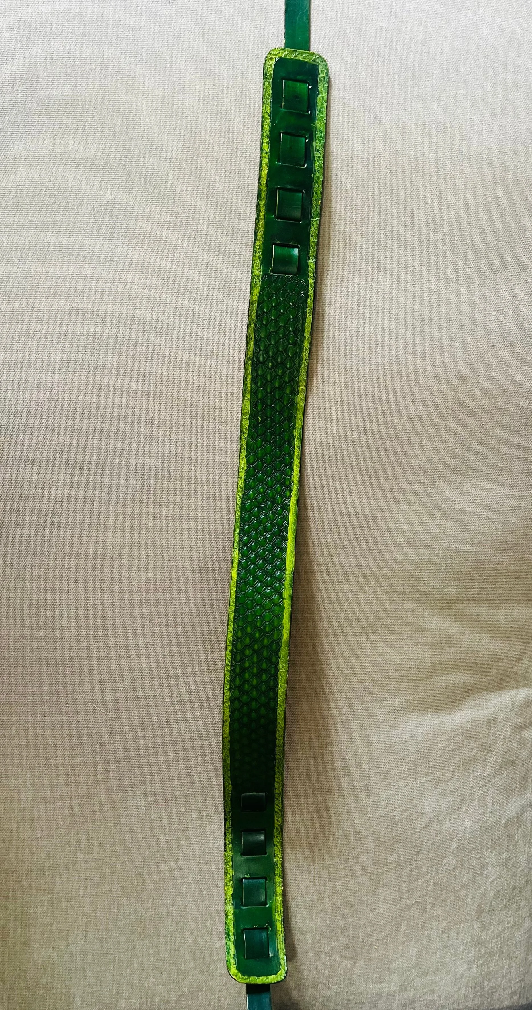 Long green LED strip light with a textured surface and a few small black connectors, mounted on a beige fabric background.