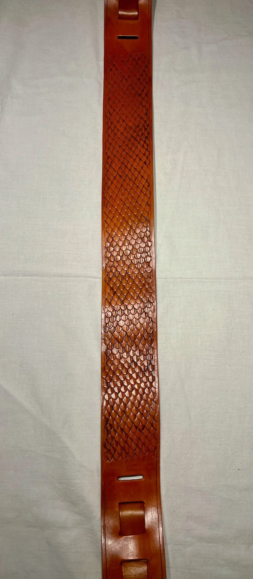 A long, narrow, orange plastic ramp with a textured surface and holes at each end, placed on a neutral-colored surface.